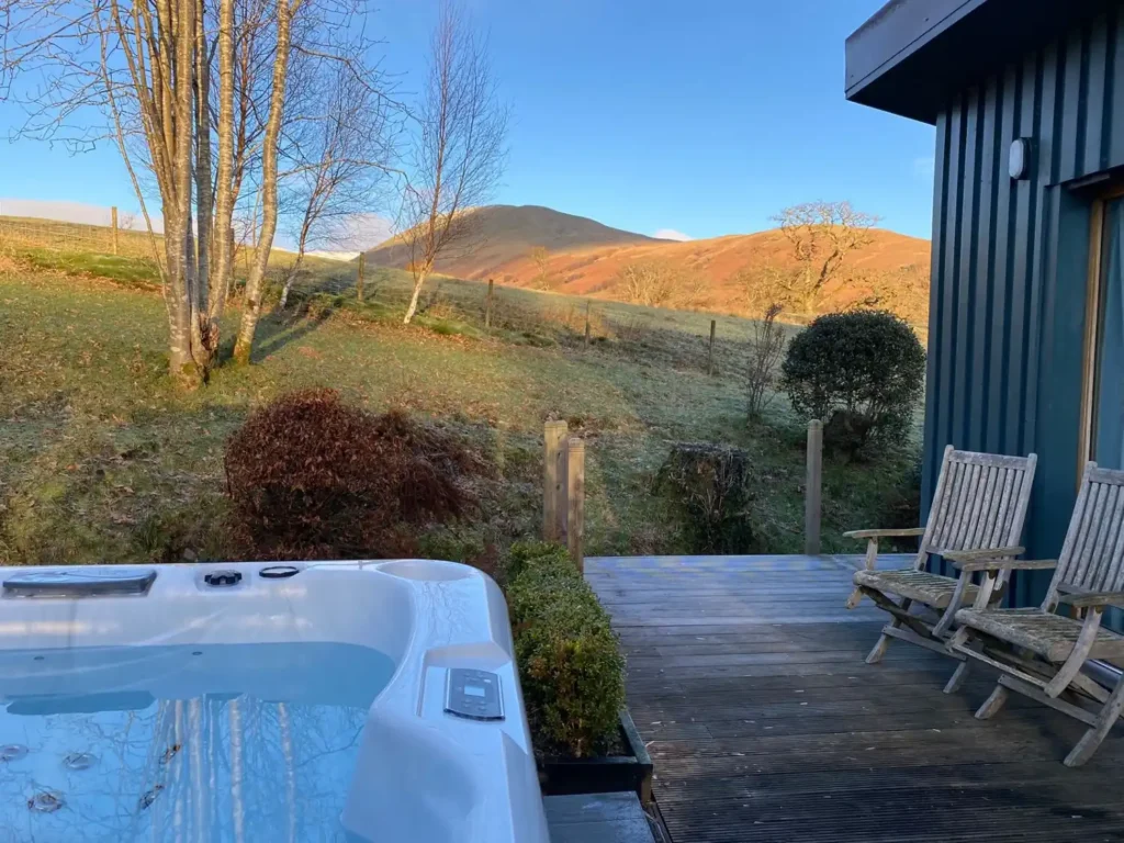 Exterior of Darroch Garden rooms in Loch Lomond showing hot tub, decking, and nearby hills.