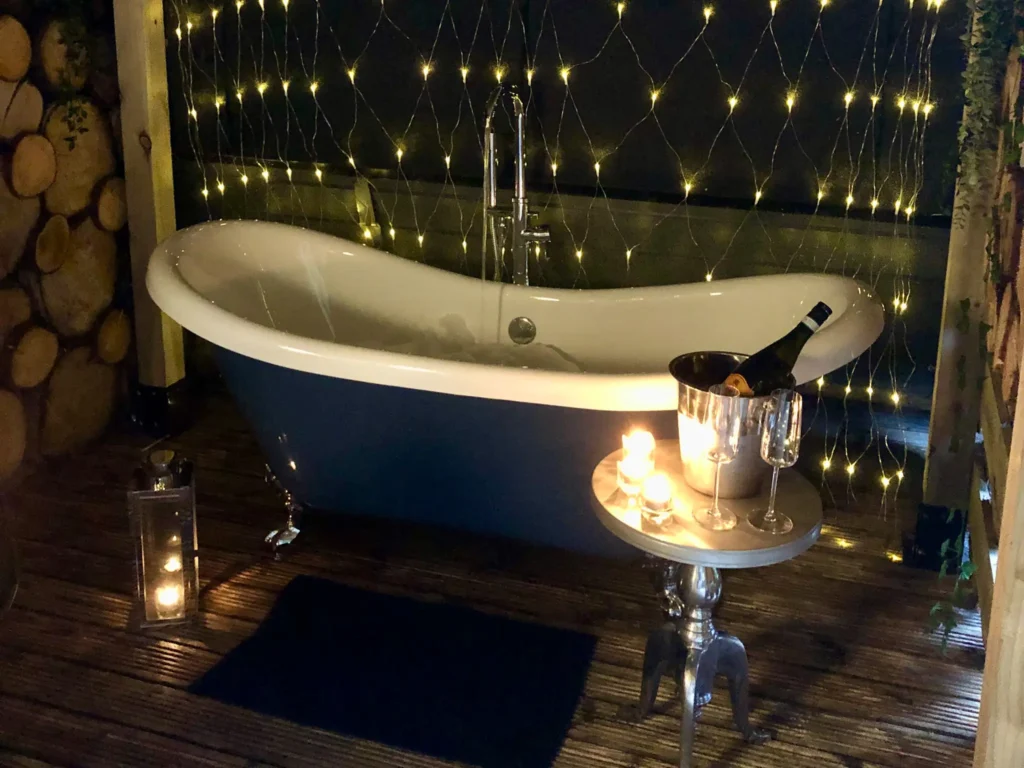 Outdoor bath tub with champagne and glasses at the side and fairy lights behind the tub.