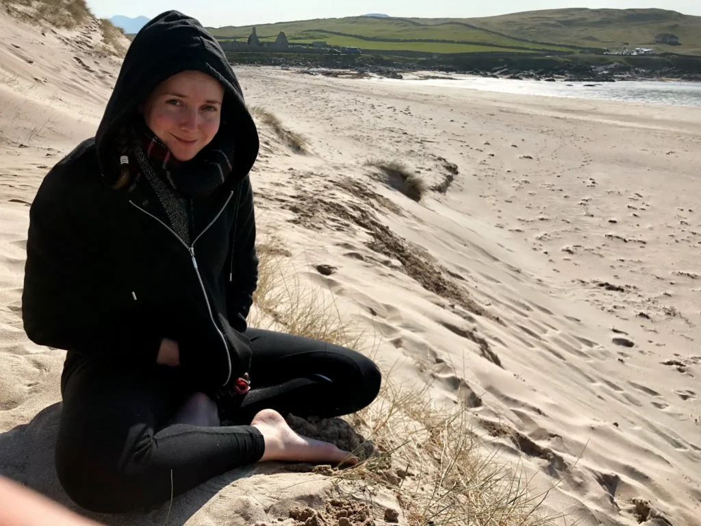 Girl wrapped up in lots of layers sitting on Balnakeil Beach on the NC500.