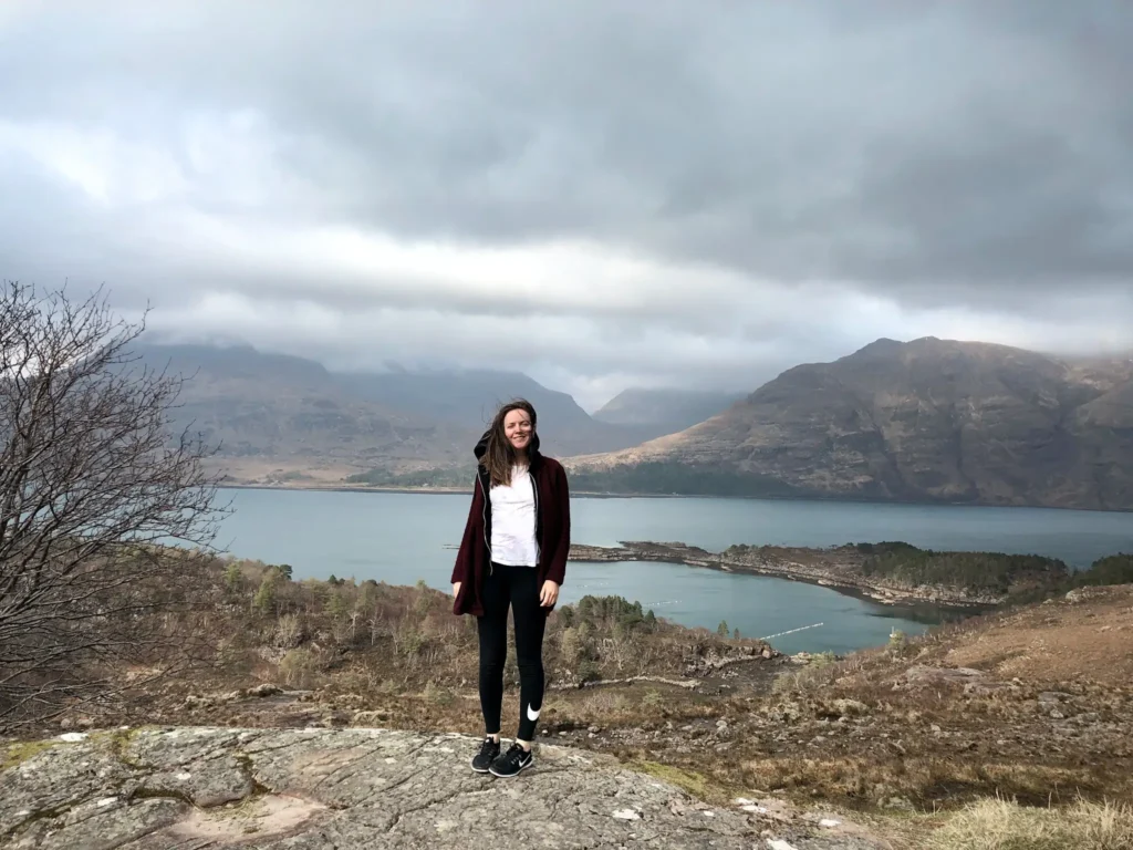 Girl looking windswept standing in front of Loch Torridon on the NC500.
