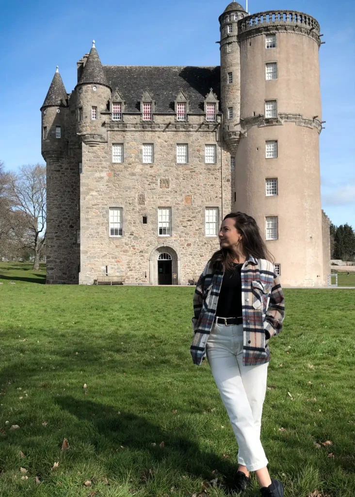Girl standing straight to the camera looking to the side with the front of Castle Fraser in the background.