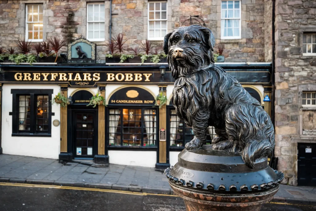Greyfriars Bobby statue with the Greyfriars bobby pub in the background in Edinburgh.