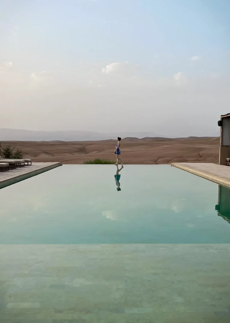 Girl walking along infinity pool edge with Agafay Desert in the background.