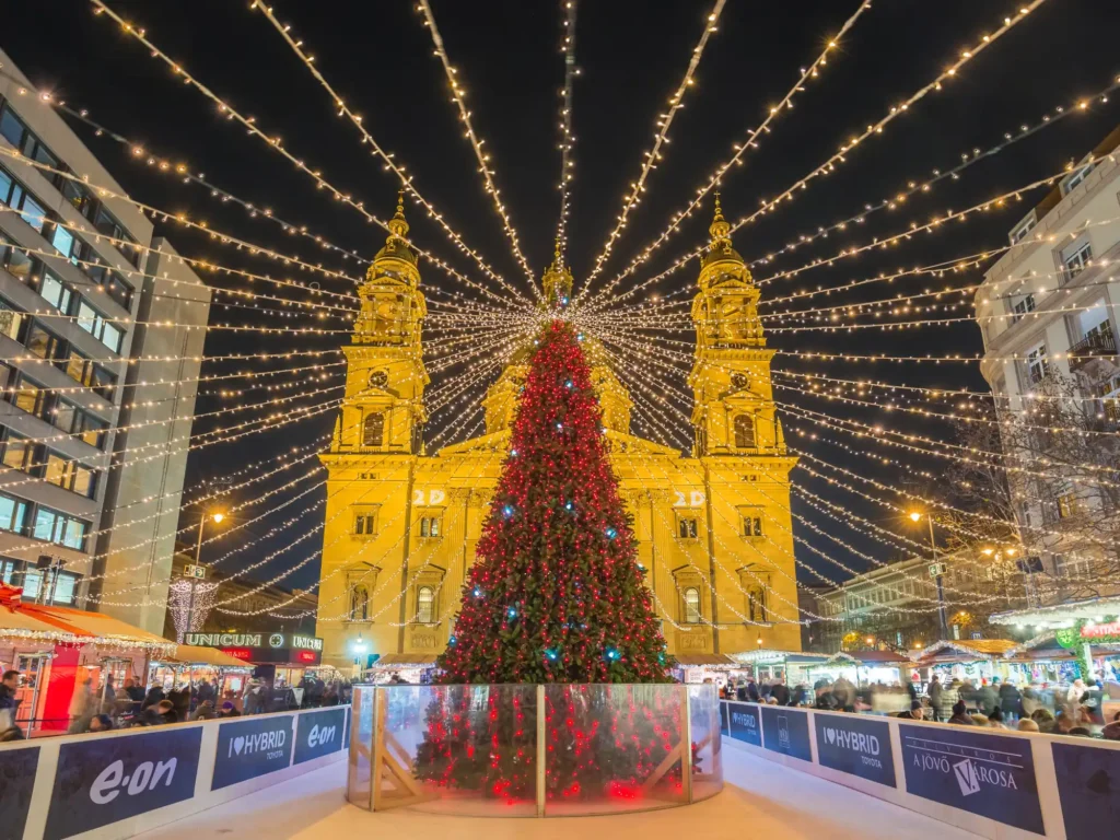 Local people and tourists enjoying the christmas markets with christmas tree, ice rink, and lights at St Stephens Basilica in Budapest.