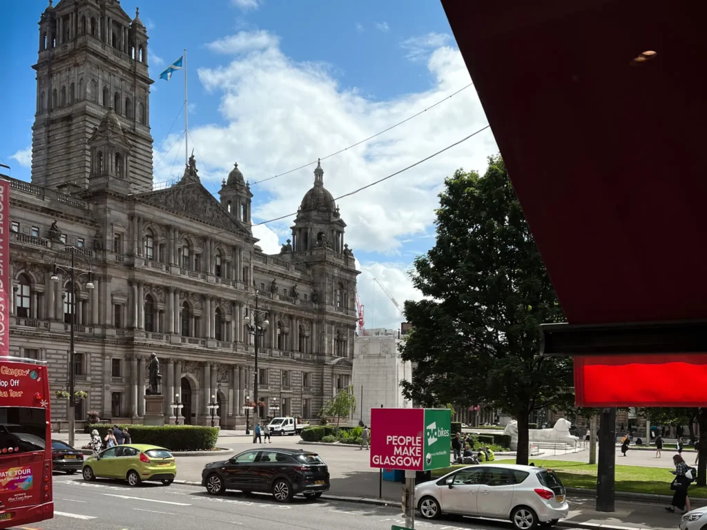 Side of view of Glasgow City Chambers on a sunny day with cars parked on the road.