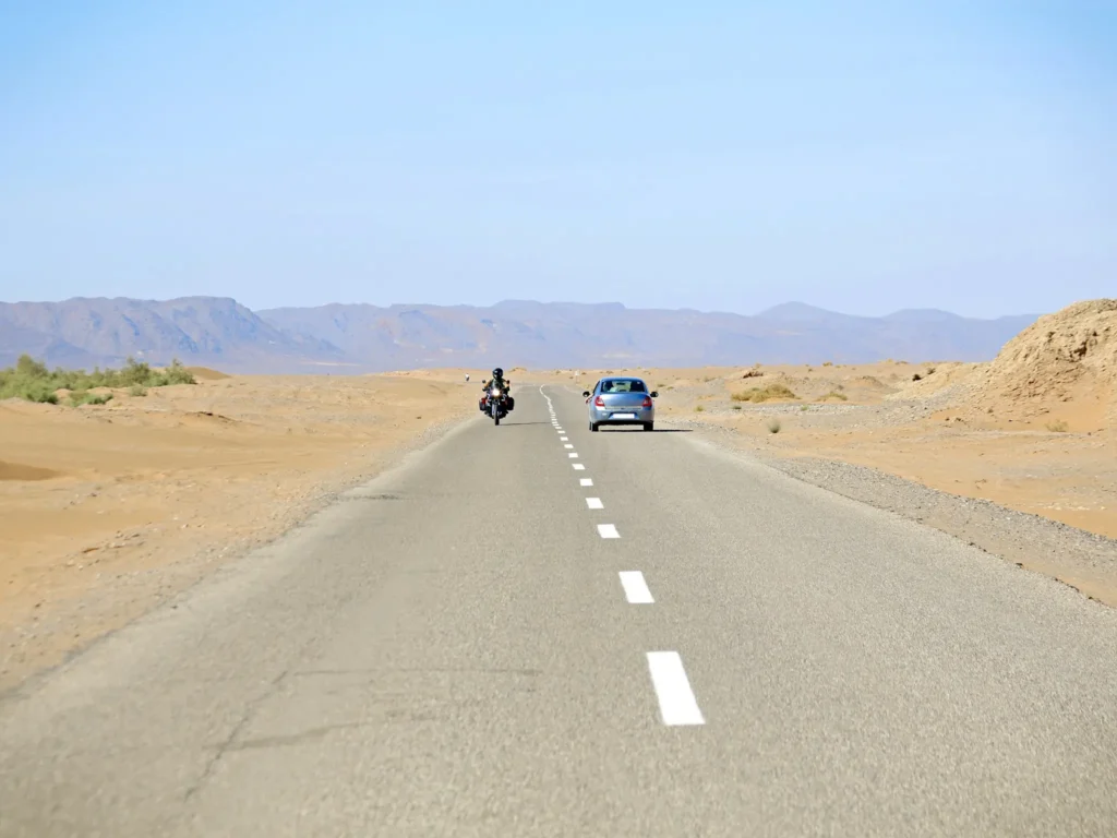 Desolate road to the Sahara Desert in Morocco with one car and one motorbike. 