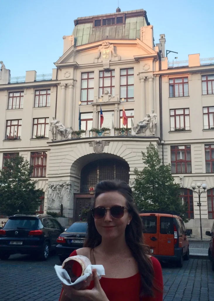 Girl wearing sunglasses and smiling at the camera in Prague holding a Trdelník pastry.
