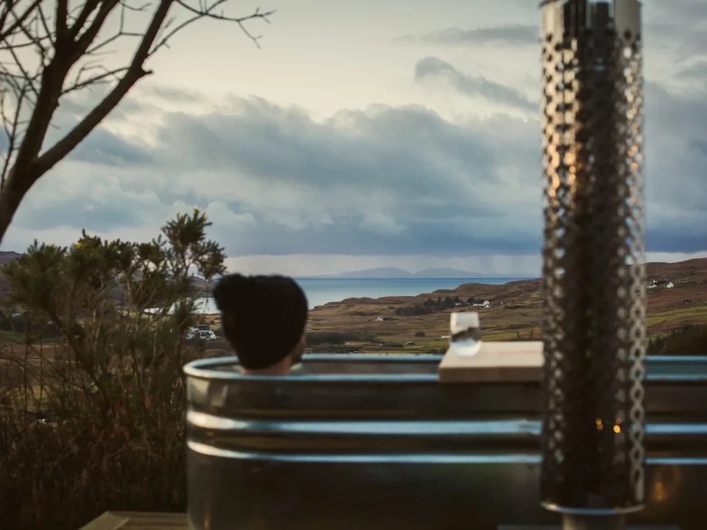 Person with hat in the outdoor soaking tub overlooking the surrounding scenery at the West Nest.