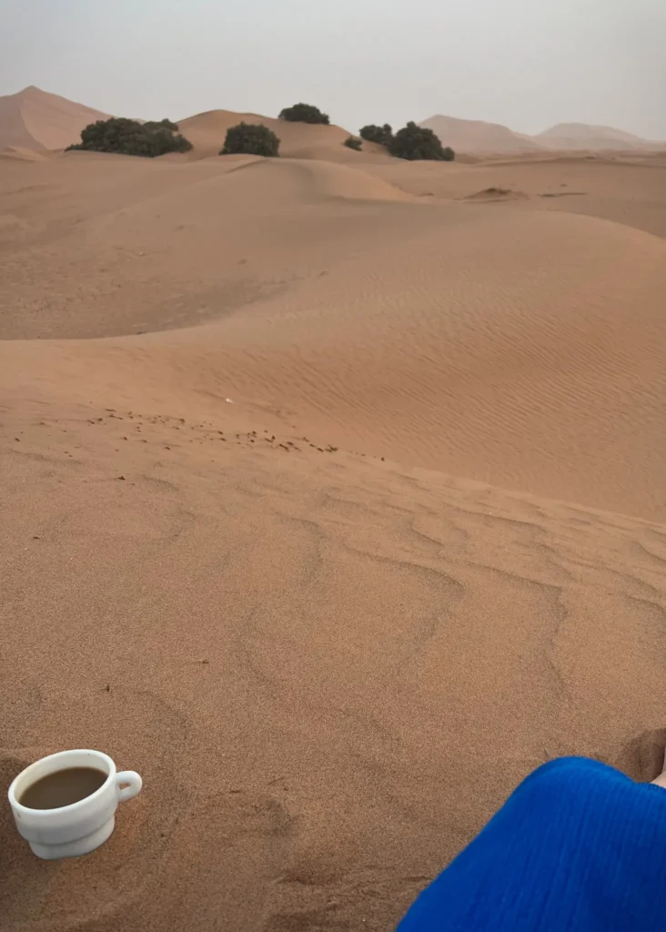 coffee cup sitting in the sand with the Sahara desert dunes in the background.