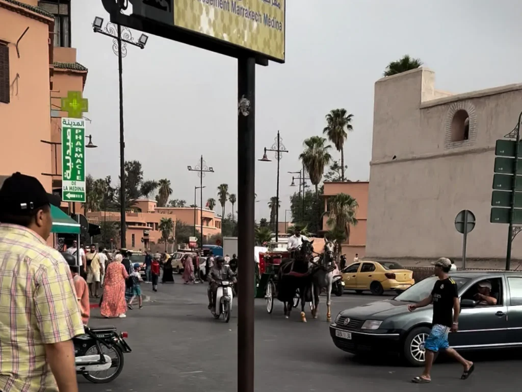 Road in Marrakech heading to the medina with cars, people, motorbikes, and horses and carriages.