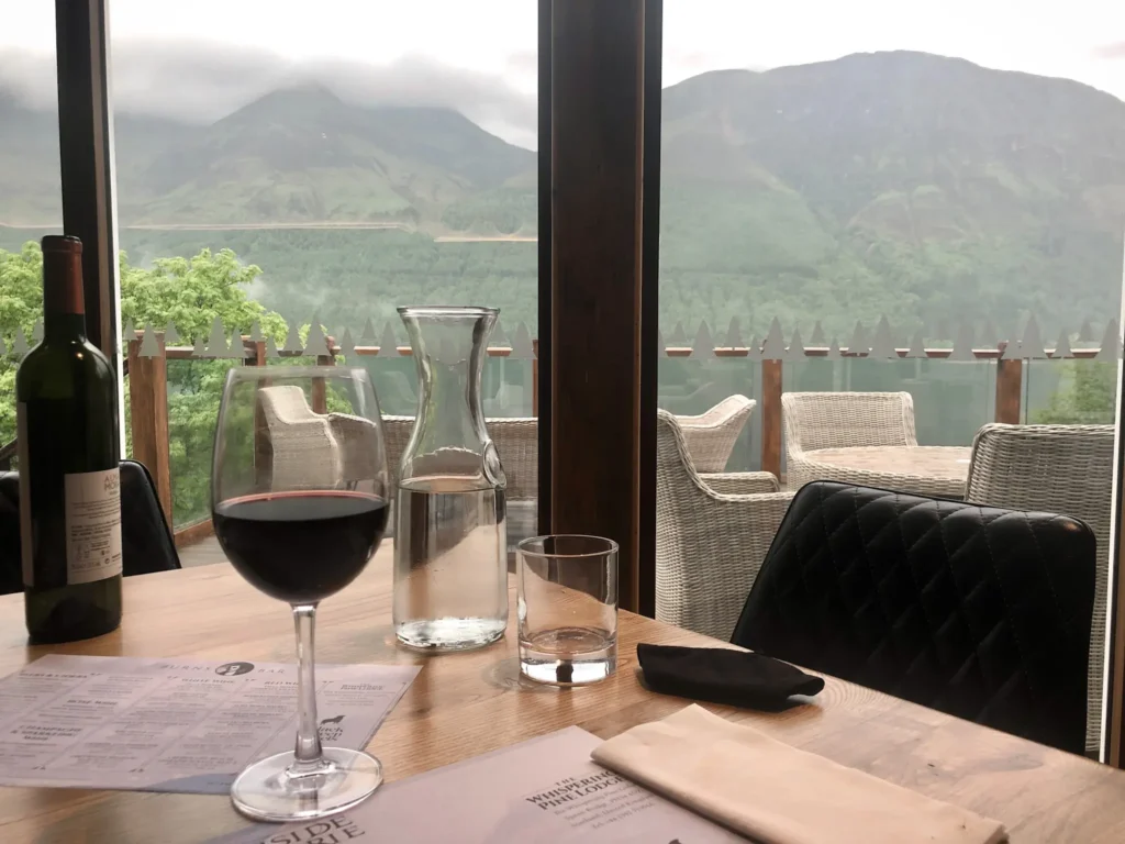 Dinner table with class of red wine and menus overlooking the nearby hills at the Whispering Pine Lodge in the Scottish Highlands.