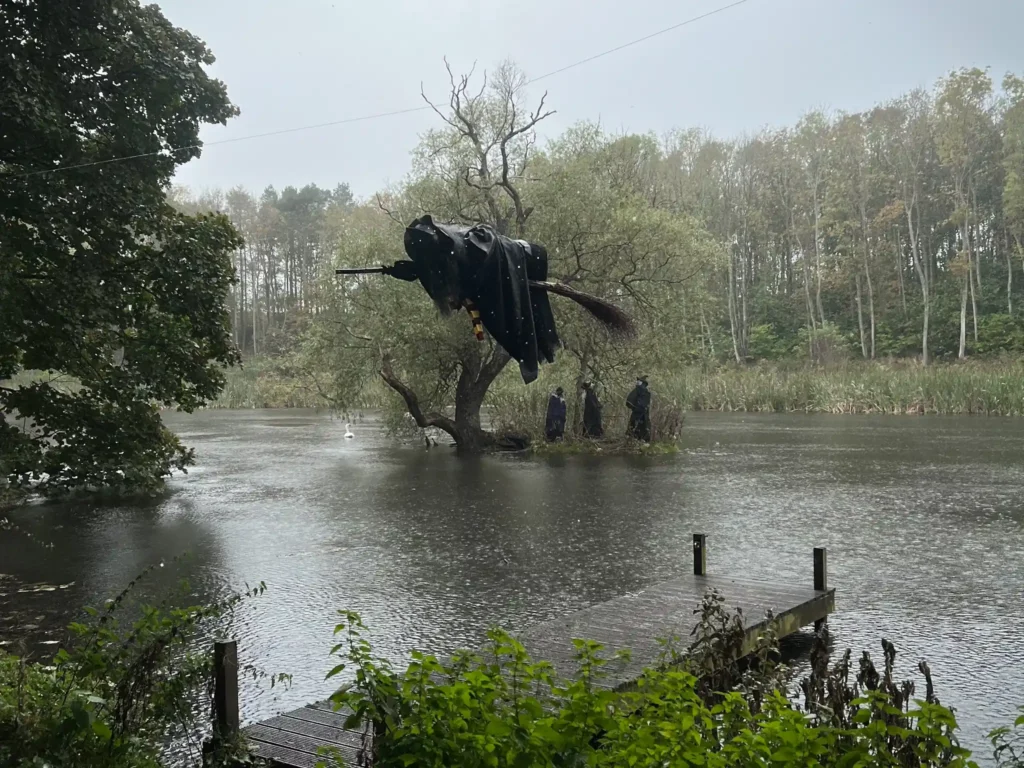 Witch on broomstick with witches on the water at Balgone Estate on a gloomy, rainy day.