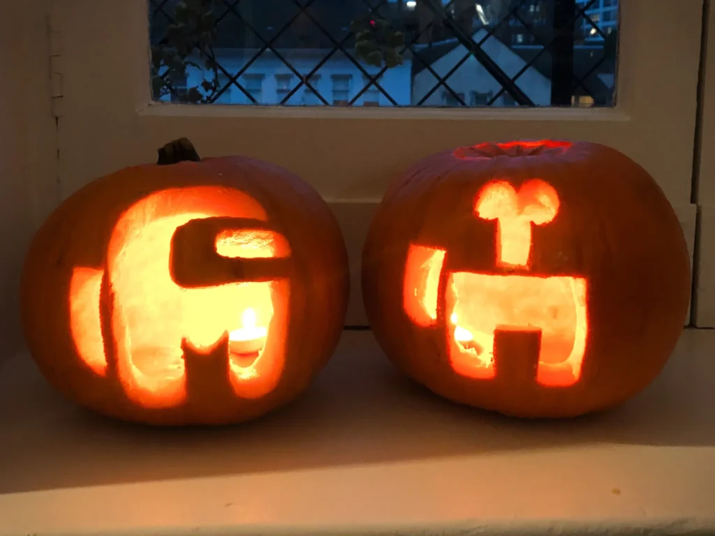 Carved pumpkins lit up in the shape of among us characters.