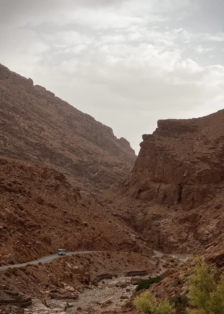 View of the Todra Gorge with minivan driving down the single track road on a cloudy day.