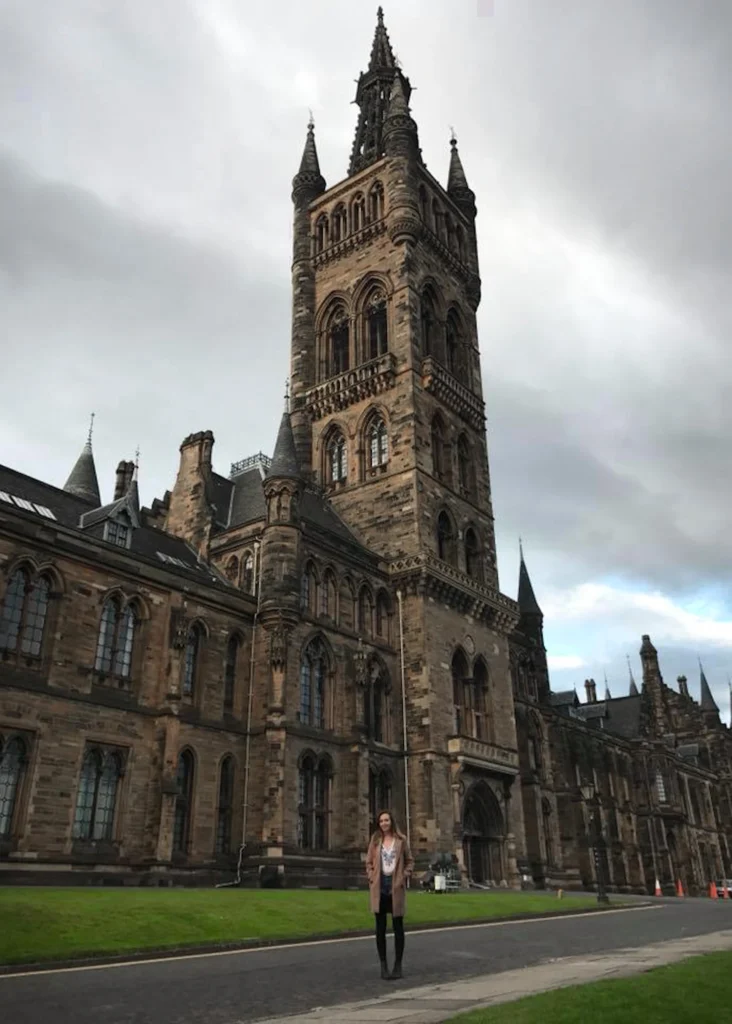 Girl standing in front of the main building of Glasgow University on a cloudy day.