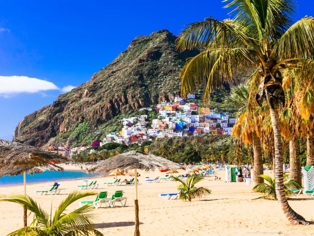 Sun loungers on the beach at las teresitas near santa cruz, canary island, spain with a houses on the hill in the background.