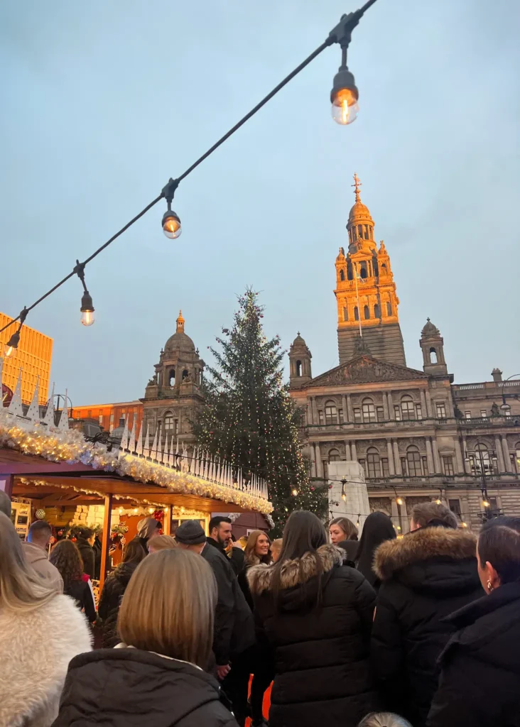 Christmas markets in George square at sunset, filled with people.