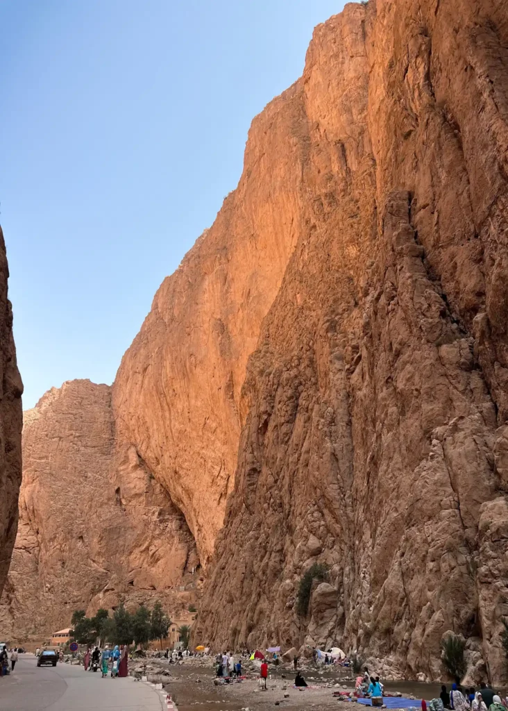 Todra Gorge in Morocco with locals and tourists in the water with the sun shining on the surrounding rock formations.