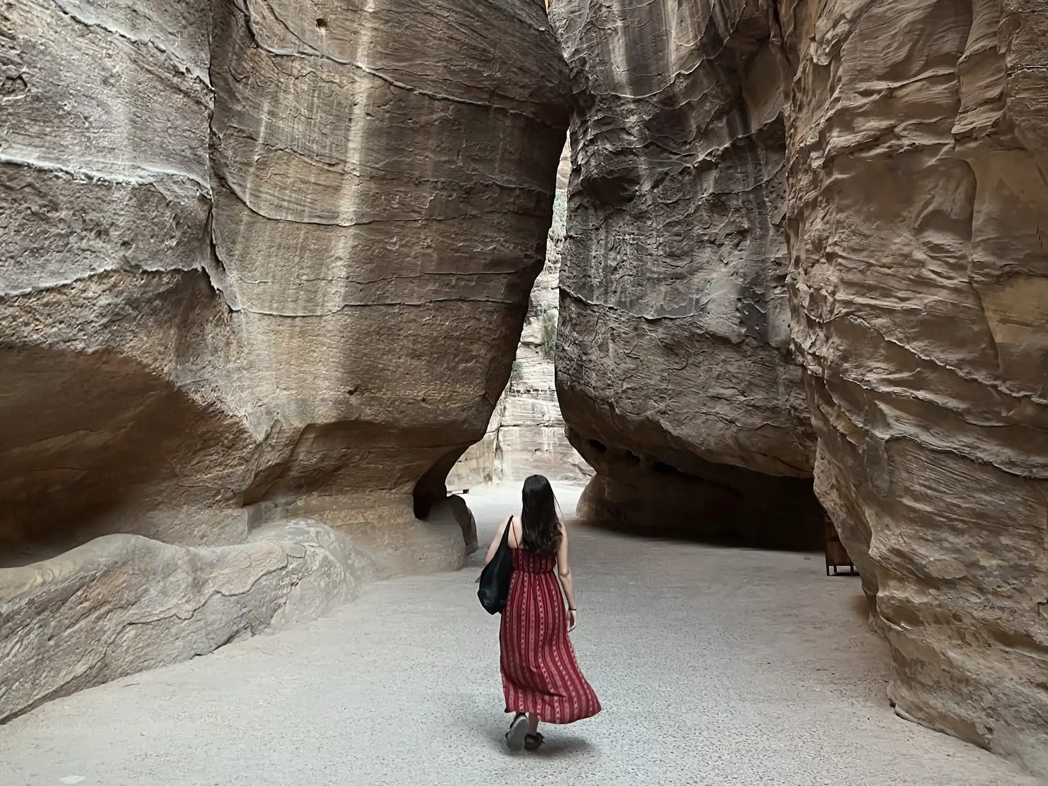 Girl walking on path carved out by the surrounding rocks on way to Petra in Jordan.
