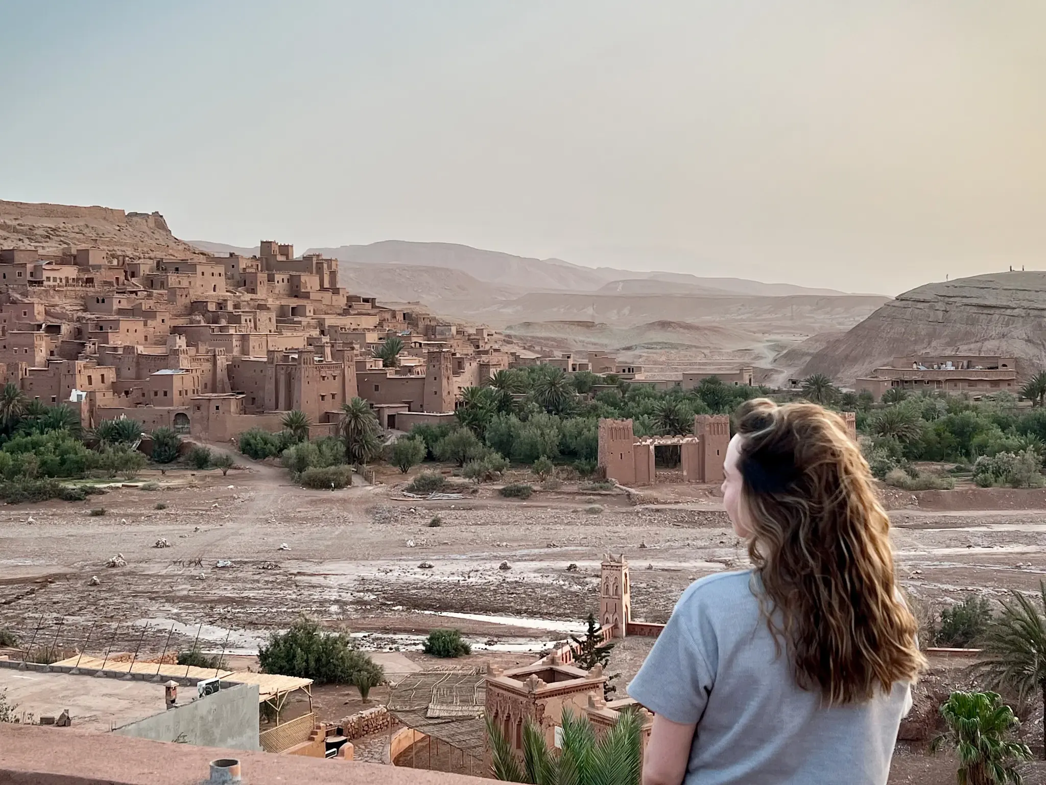 Girl standing on a balcony overlooking Ait Ben Haddou at sunrise.