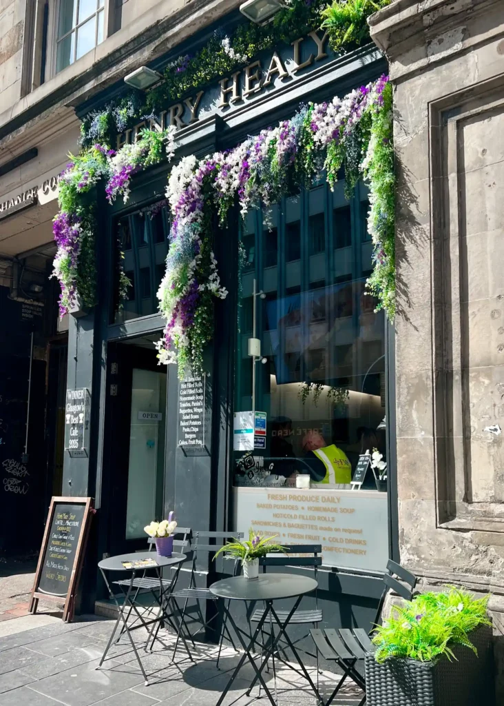 Facade of Henry Healy's on Queen Street in Glasgow with flowers around the sign and outdoor seating