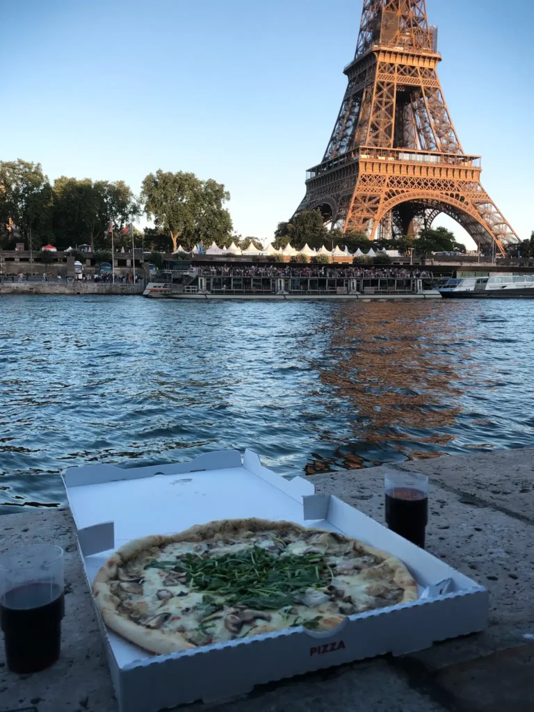 Takeaway pizza sitting by the River Seine in Paris with eiffel tower in the background.