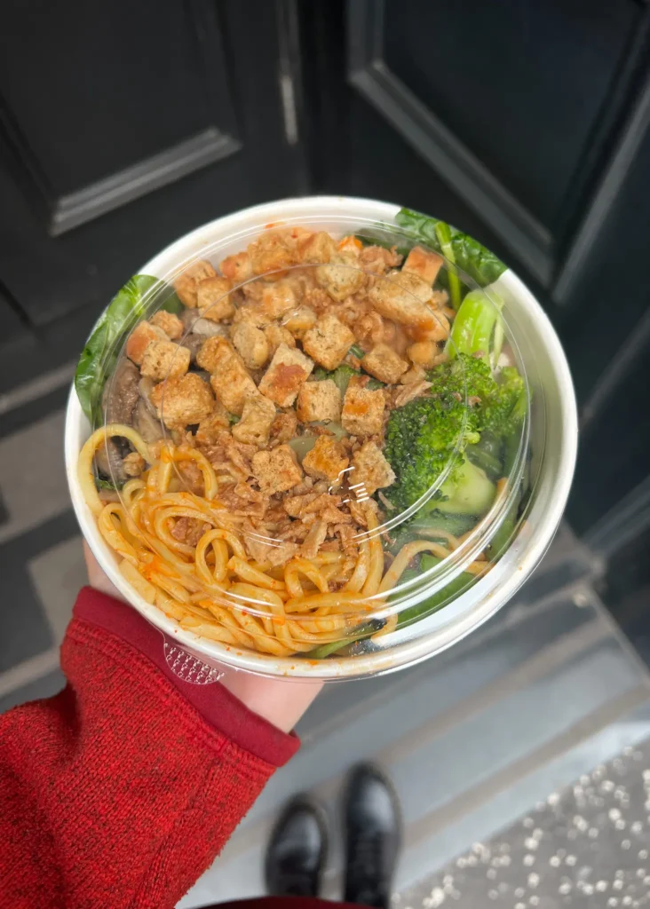 Holding a bowl from Sprigg in Glasgow city filled with noodles, croutons, broccoli.