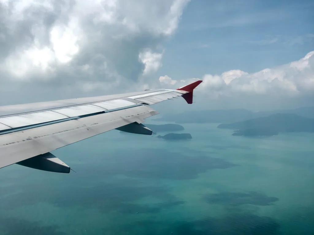 Plane wing flying over turquoise sea and islands below.