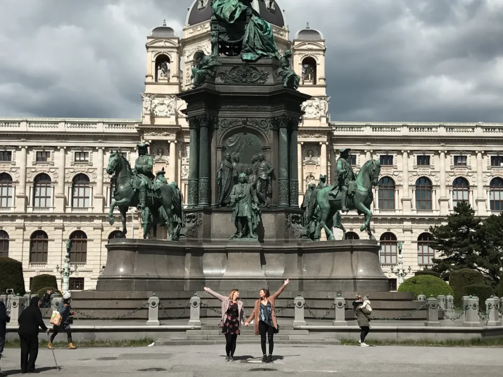 Two girls holding hands looking at each other with arms in the air at MuseumsQuartier in Vienna.