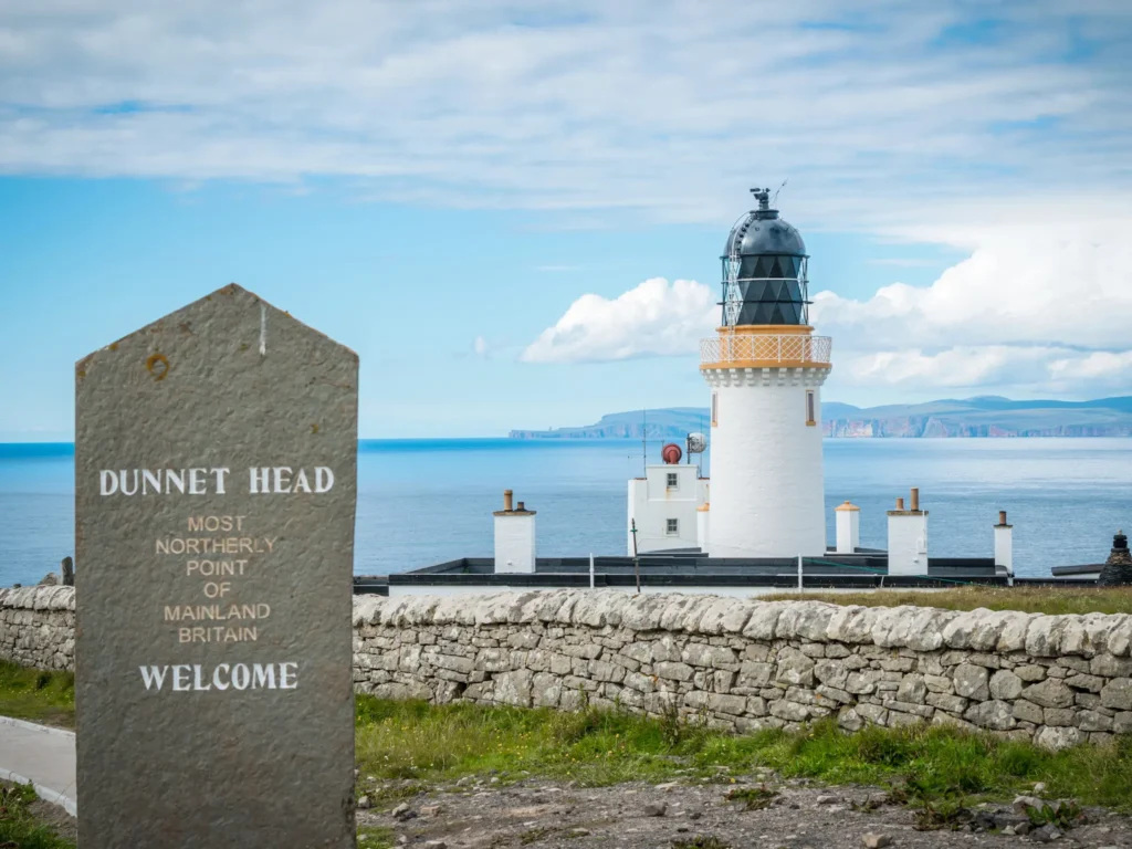 Dunnet head sign with lighthouse in the background and the Orkney islands.