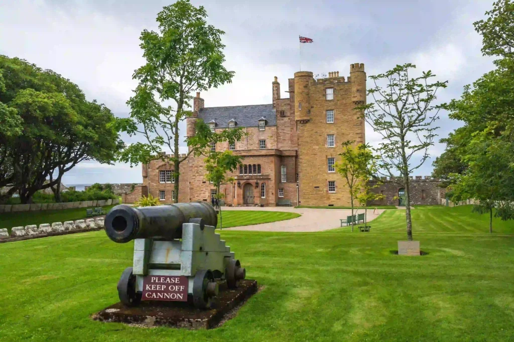 Castle of Mey with cannon in front and landscaped grounds on a cloudy day in Scotland.