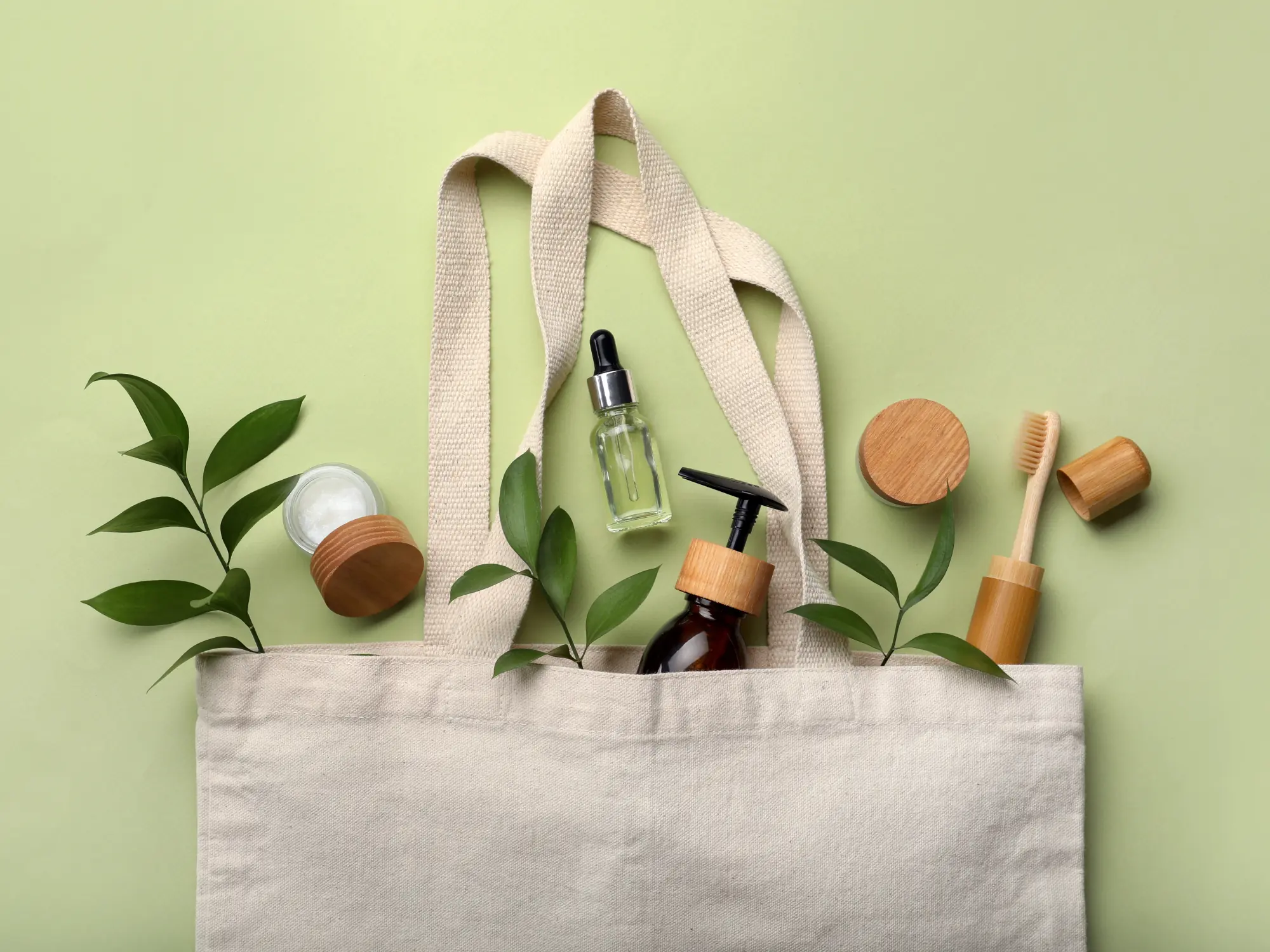 Bag with eco friendly products on green background, flat lay