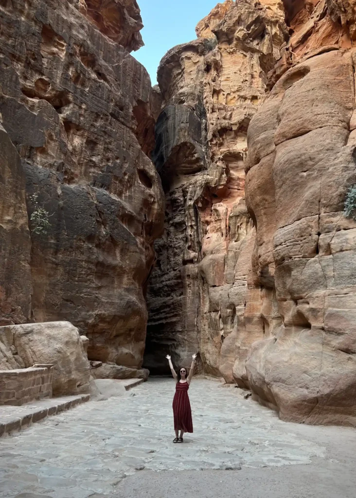 Girl standing with hands up in the middle of a canyon on way to Petra in Jordan.