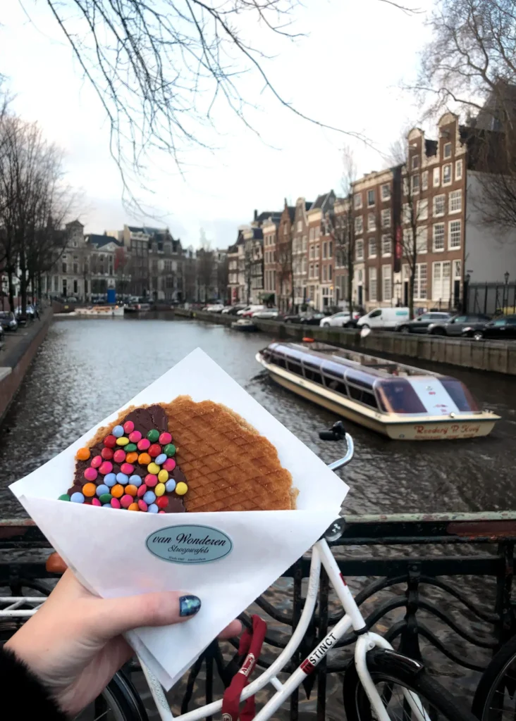 Holding a stroopwafel with a boat going down the Amsterdam canal in the background