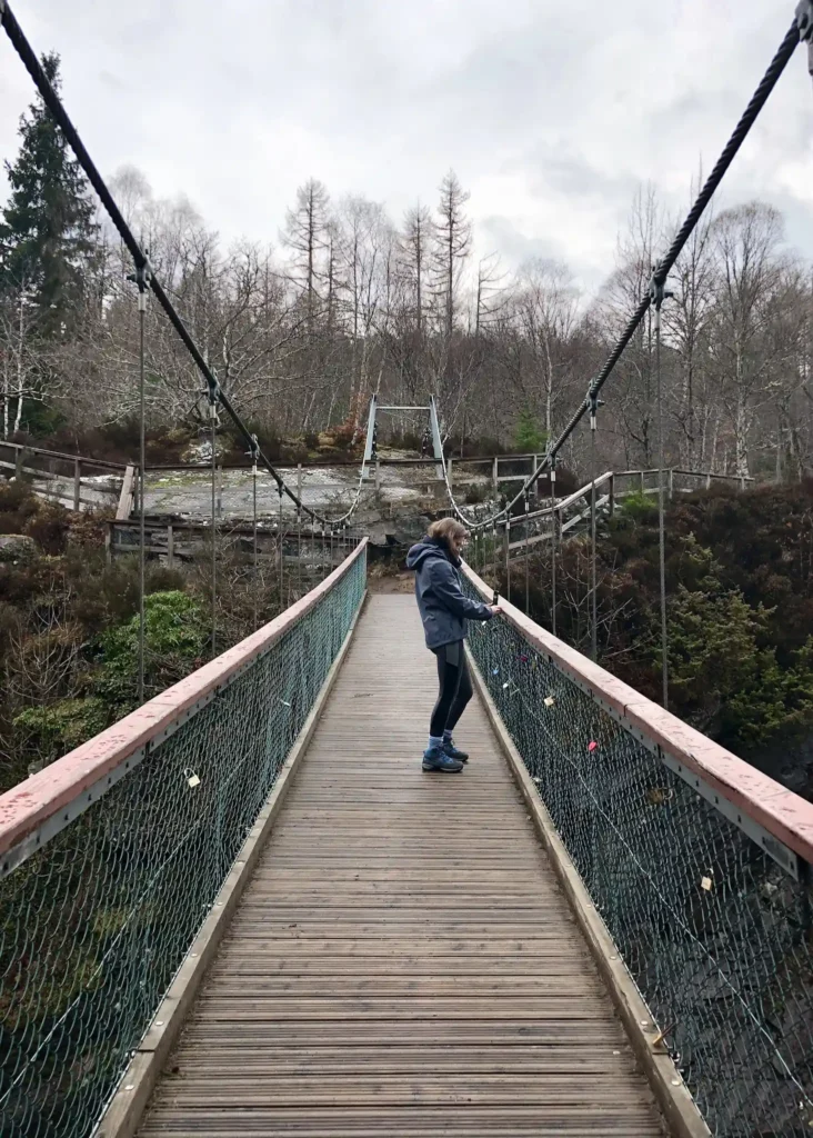 The suspension bridge over rogie falls with girl in the middle taking a picture.