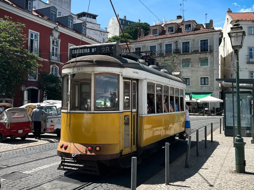 Tram 28 travelling down a street in Lisbon on a sunny day.
