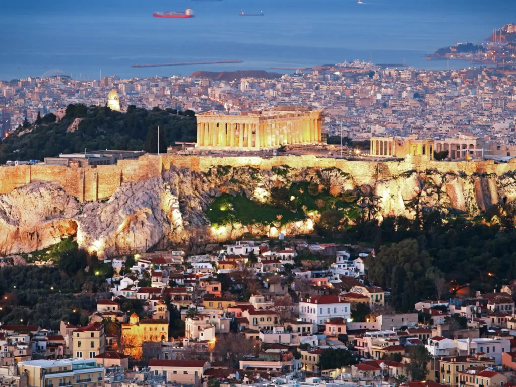 Cityscape of athens with illuminated acropolis hill, pathenon and sea at night, greece