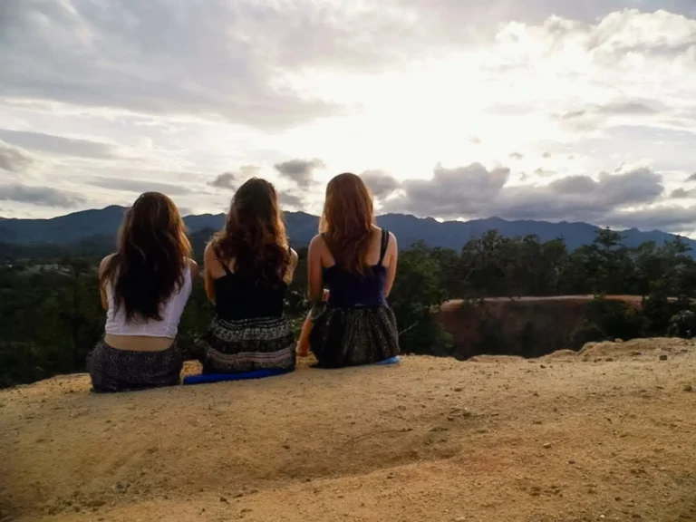 Three girls sitting with their backs to the camera watching the sunset at Pai Canyon in Thailand.
