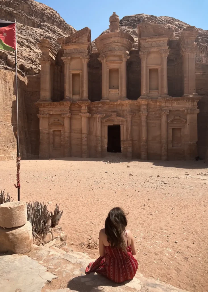 Girl with back to the camera sitting looking at the monastery at Petra in Jordan.