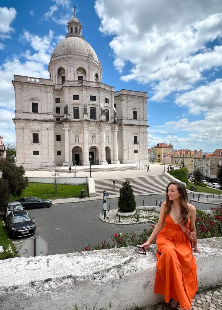Girl in orange dress sitting on a wall with the National Pantheon in Lisbon in the background.