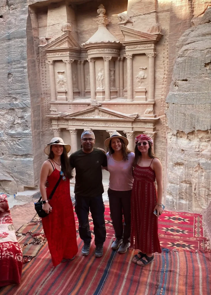Four travellers smiling at the camera with Petra in Jordan in the background.
