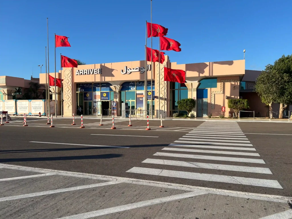 Exterior of Agadir Airport on a sunny day with Moroccan flags flying.