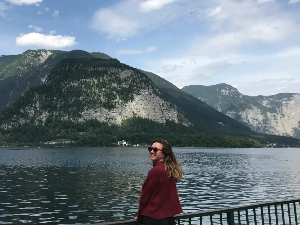 Girl standing at the edge of Hallstatter See with mountains in the background.
