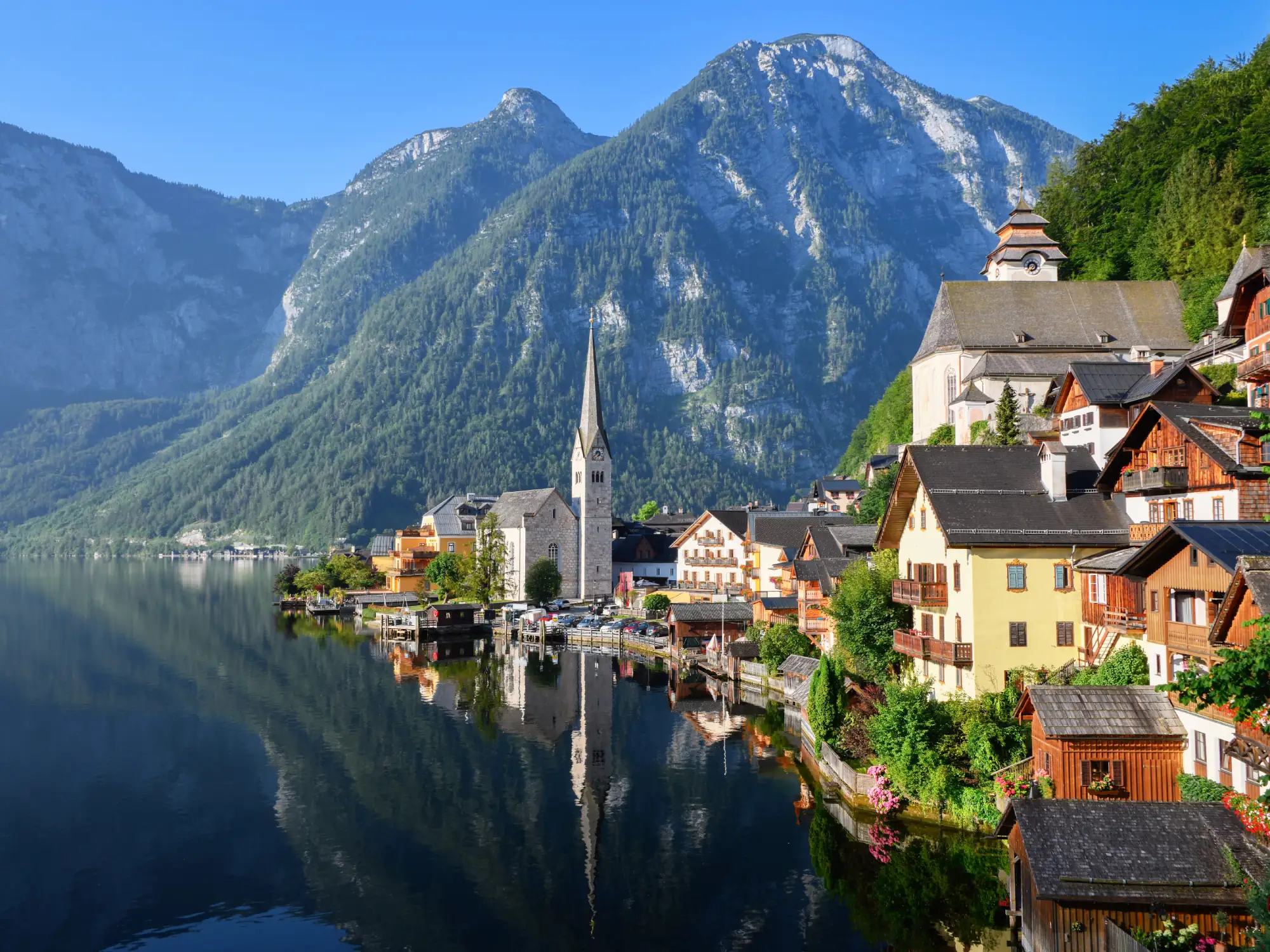 Hallstatt village with church with reflection in the still water of the lake with alps mountains in the background in austria.