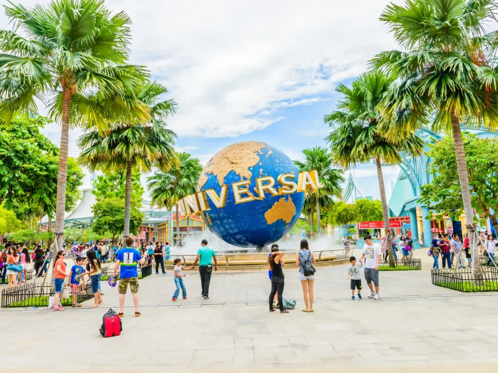 Tourists and theme park visitors taking pictures of the large rotating globe fountain in front of Universal Studios on Sentosa island, Singapore.