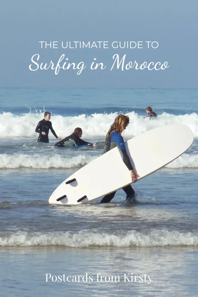 Pinterest Pin showing girl walking in sea with her surfboard with learners behind her. There's text over the top reading "The Ultimate Guide to Surfing in Morocco" and "Postcards from Kirsty"