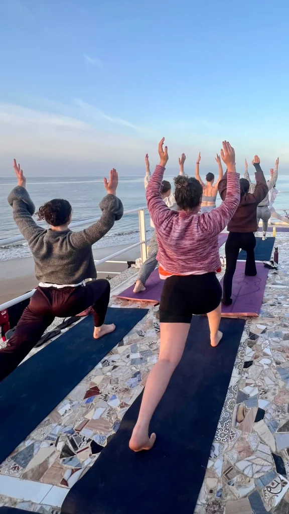 People practicing yoga on the rooftop terrace of Surf Coast Morocco with the Atlantic Ocean in the background.