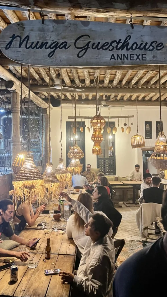 Munga Guesthouse Annexe in Taghzout, Morocco at night with lights on and people sitting, drinking, and socialising.
