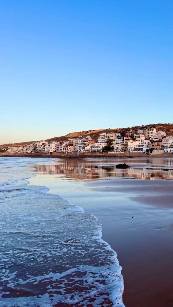 Taghazout at sunrise as a wave is coming in and the houses in the background. 