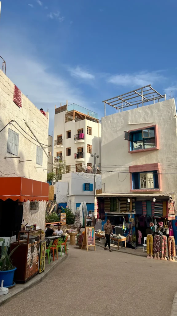 View down a street in Taghazout showing restaurants with outdoor seating and tourist shops.
